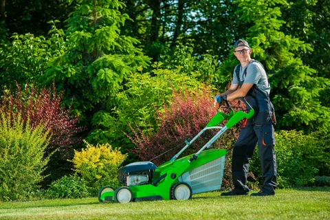 Professional gardener in overalls and glasses standing with a bright green lawnmower, focused on garden cleaning and lawn maintenance in a lush Toronto residential yard.