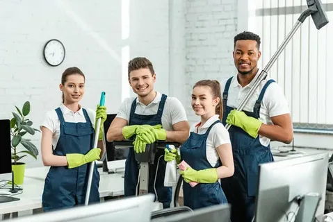 A team of four uniformed house cleaners in Toronto working together to clean a large, brightly lit residential interior, highlighting comprehensive, multi-person cleaning service.