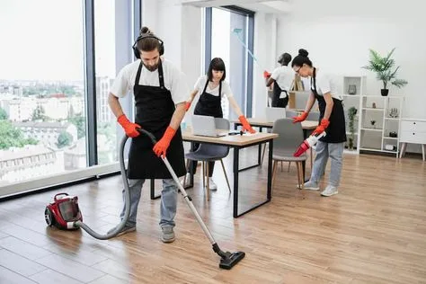 Eco Techno Clean team providing professional house cleaning in Toronto, with a male cleaner vacuuming a wood floor and two female cleaners dusting an office desk.